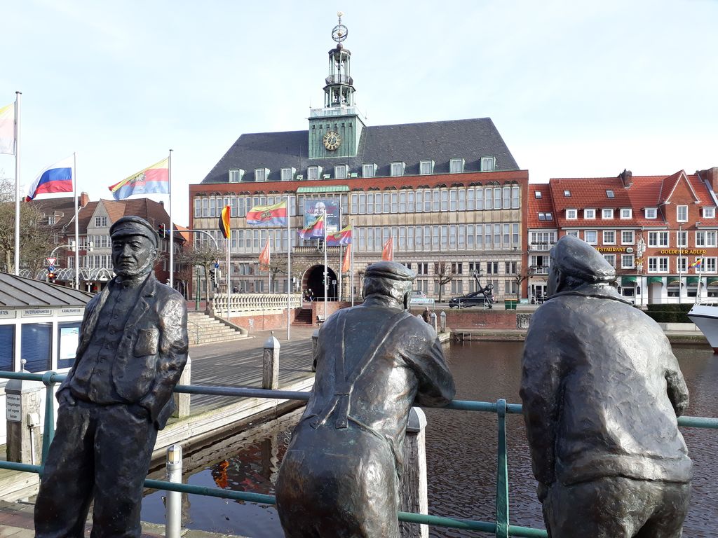 Man sieht Hinni den Delftspucker und seine beiden Freunde Jan und Joke. Drei Bronzefiguren, welche oberhalb des Ratsdelftes stehen. Im Hintergrund das ostfriesische Landesmuseum