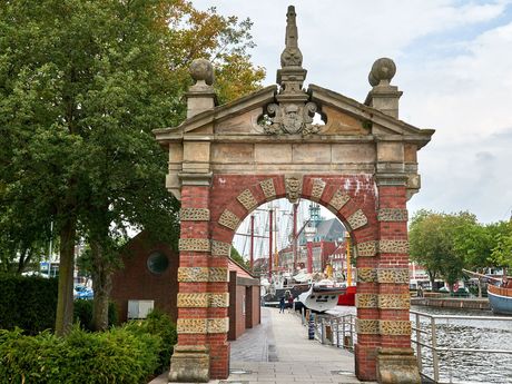 Zu sehen ist das Emder Hafentor mit Blick richtung Innenstadt. Schaut man durch das Tor sieht man den Segler Heureka, Teile des Feuerschiffes und des Ostfriesischen Landesmuseums