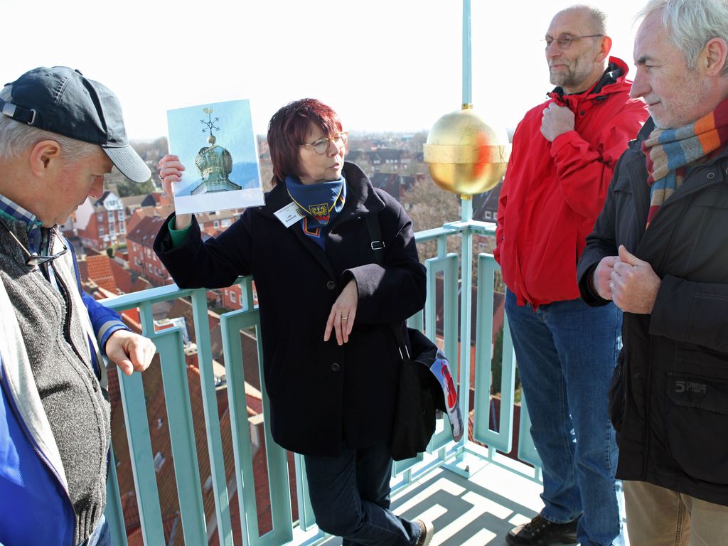 Eine Stadtführerin steht mit einer Gruppe auf dem Rathausturm und erzählt geschichtliches zu Emden