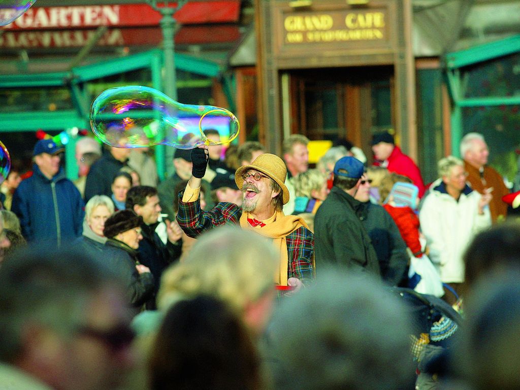 Verkleideter Seifenblasenkünstler macht eine riesen Seifenblase inmitten einer zuschauenden Menschenmenge