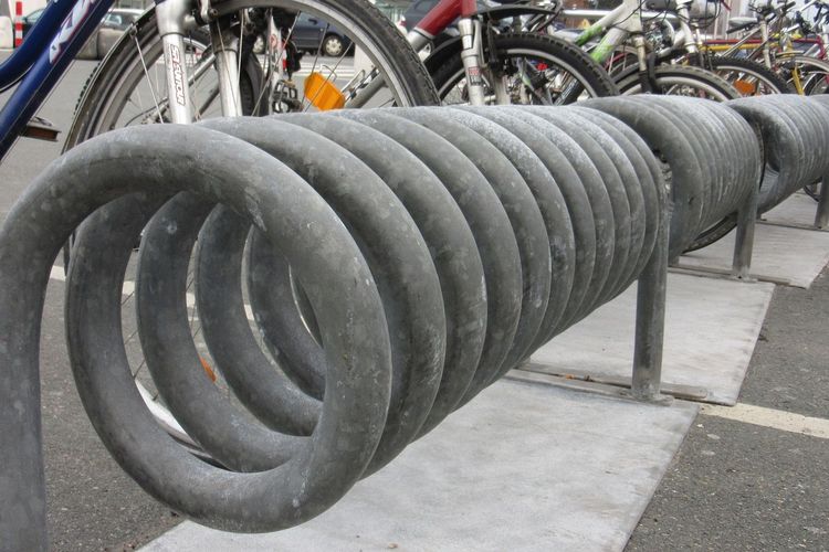 Zu sehen ist ein spiralförmiger Fahrradständer im Vordergrund und Teile abgestellter Fahrräder