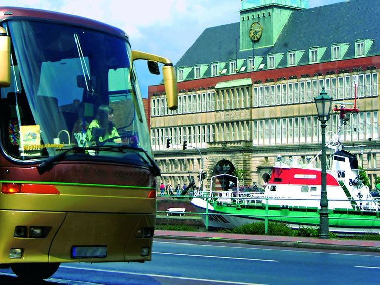 Die Front eines Reisebusses seitlich im Bild. Im Hintergrund der Seenotrettungskreuzer Georg Breusing und das Ostfriesische Landesmuseum