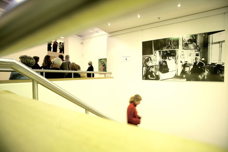 Sehr helle Aufnahme von der Kunsthalle von innen. Eine Person geht eine Treppe runter, eine Personengruppe im Hintergrund schaut sich Bilder an